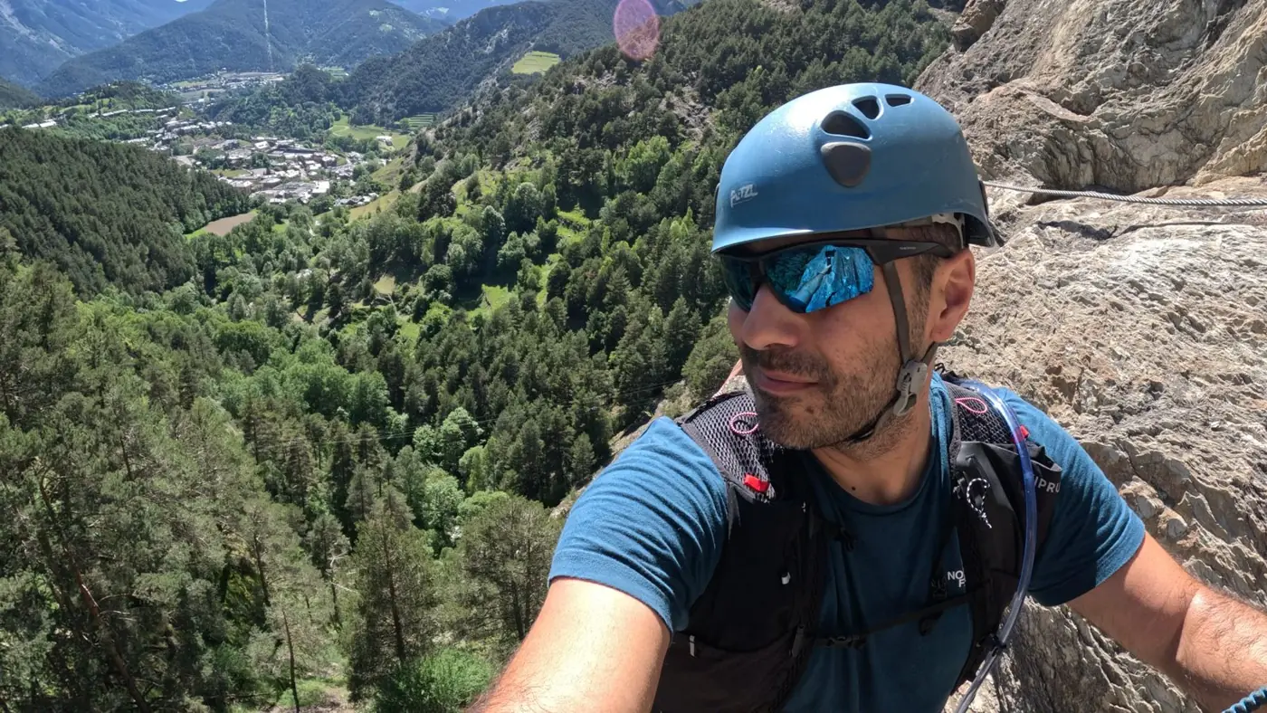 Gabriel con casco en una vía ferrata, con el valle de Ordino al fondo